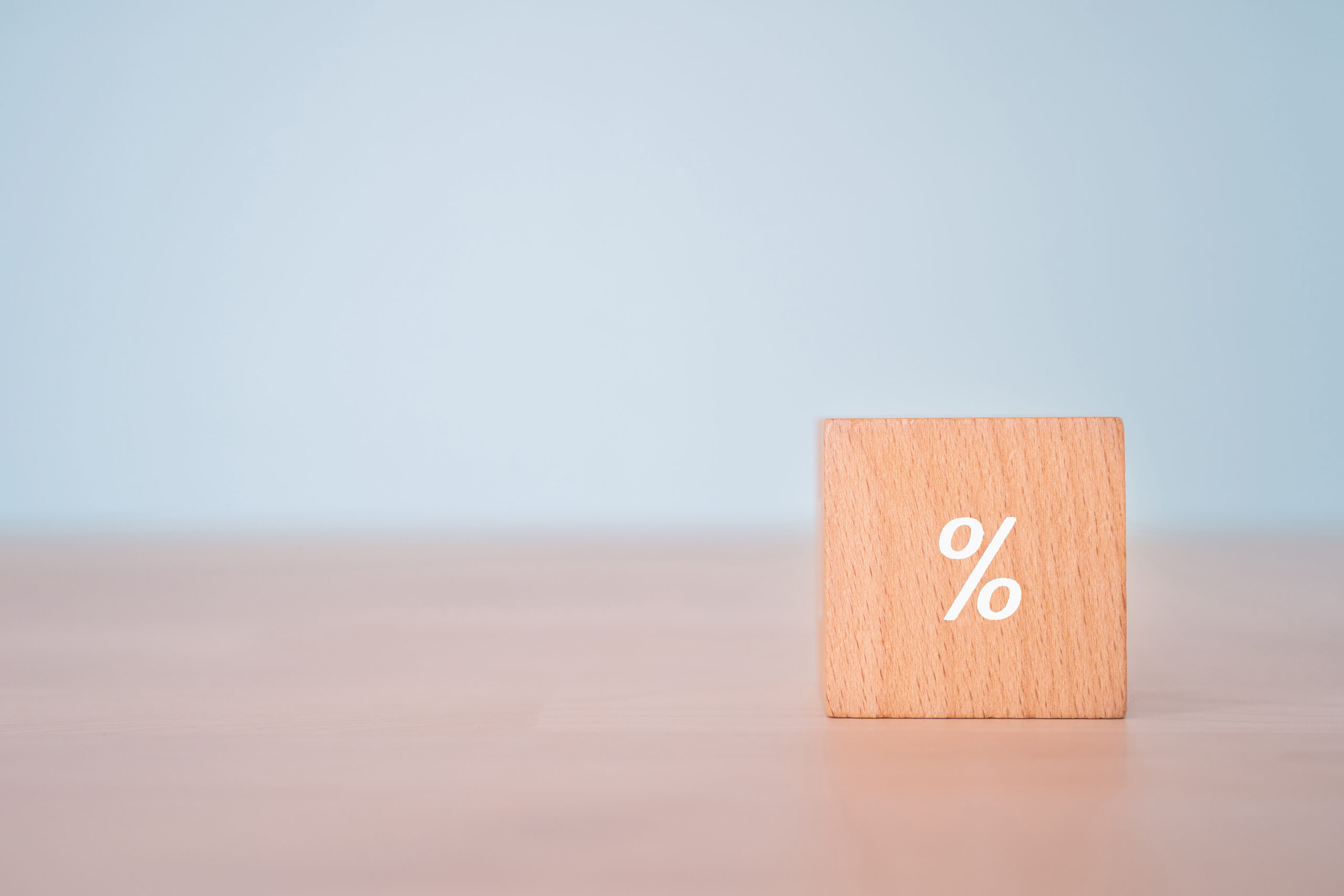 Wooden block with white percentage sign indicating interest rates on wooden table with blue background, economy